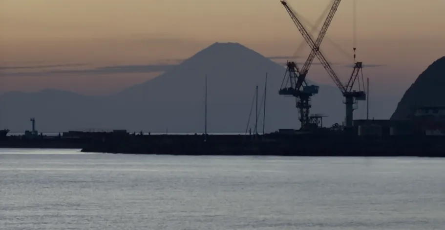 夕暮れの空に浮かぶ富士山のシルエットと、港のクレーン