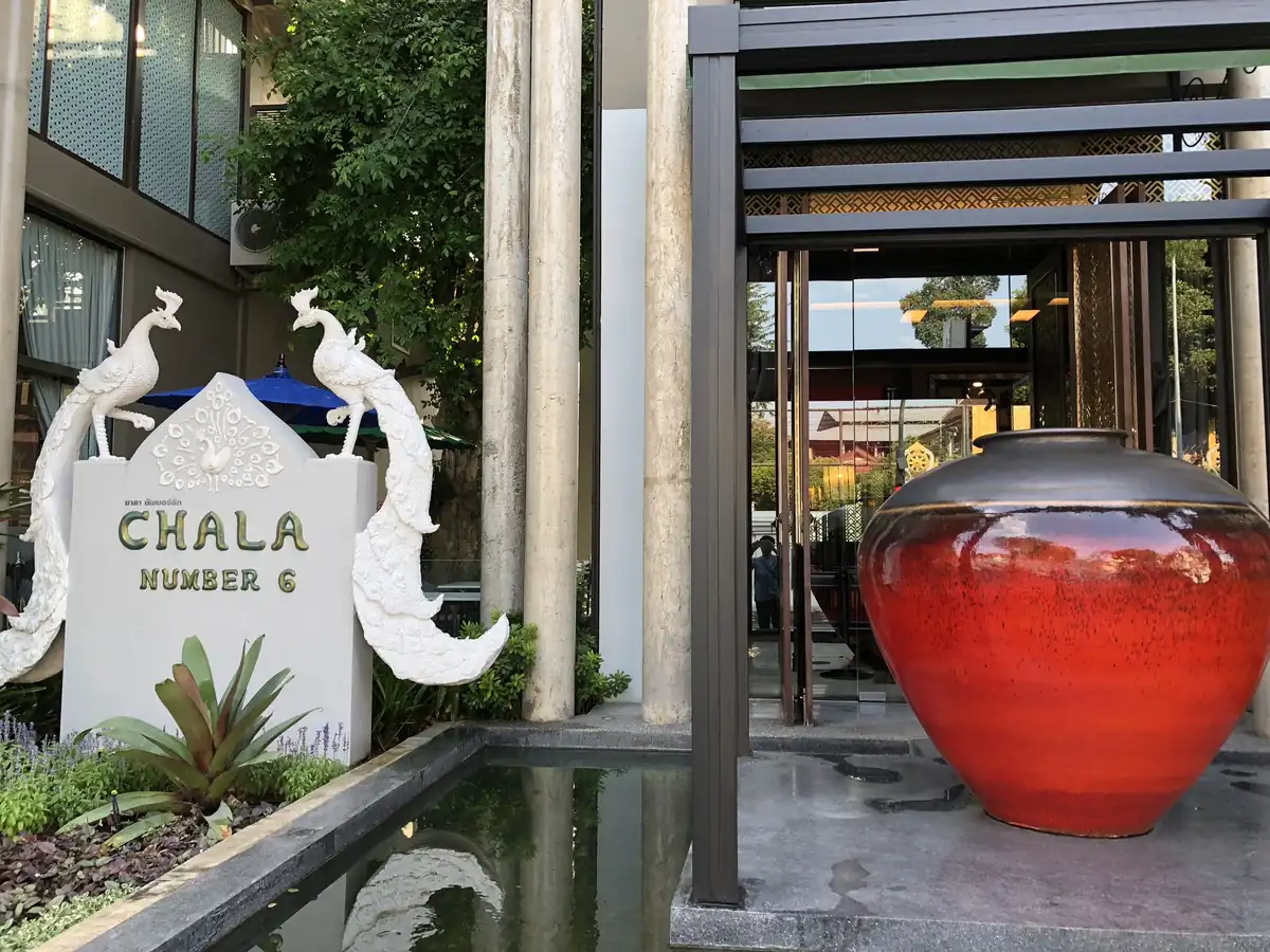 CHALA NUMBER 6の看板と白い孔雀の像、赤い大きな壺