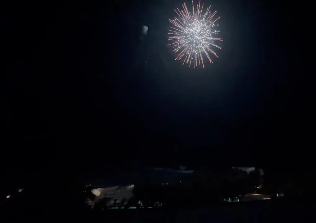 夜空に上がる花火と、明かりのついたホテルの客室棟