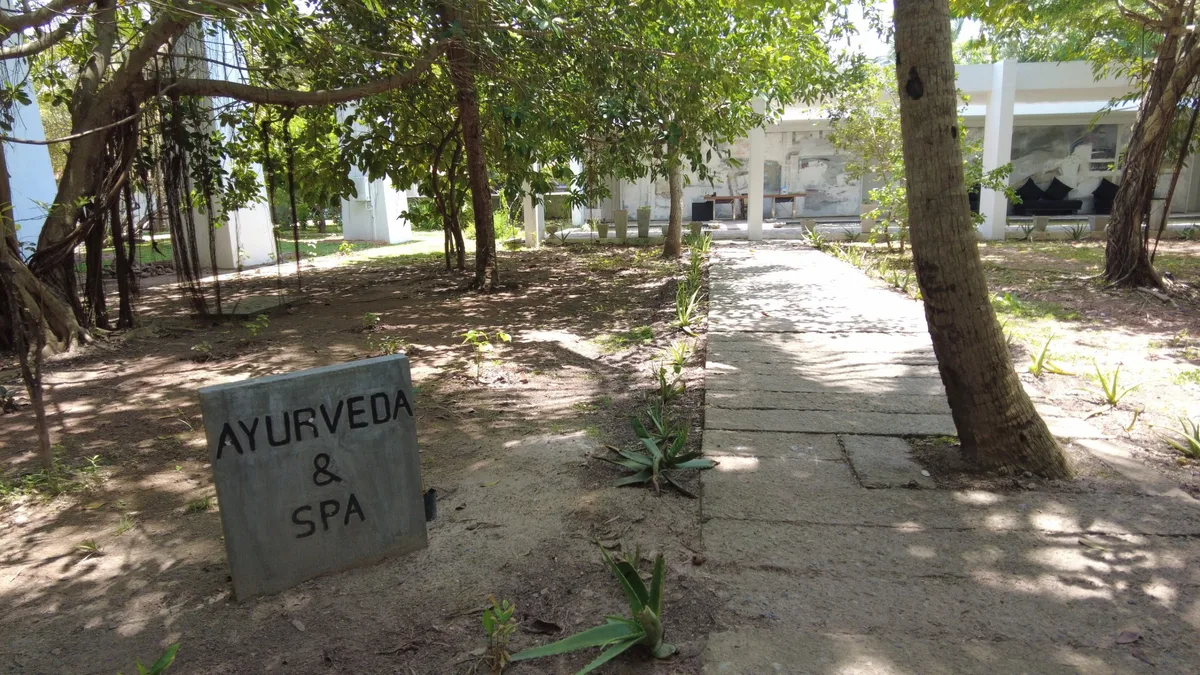 木陰に置かれた「AYURVEDA & SPA」の看板と、奥へ続く小道