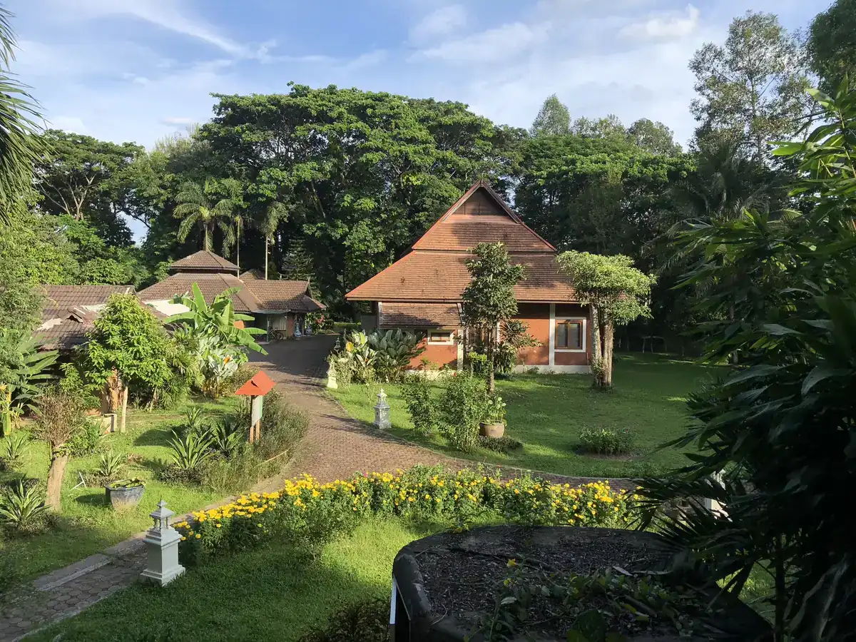 芝生と花壇の向こうに並ぶ、タイ風の屋根のコテージ